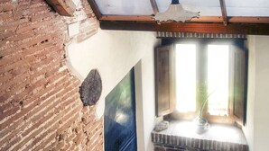 A room with a brick wall, a window with a view, a ceiling fan, and a fire extinguisher. - Holiday apartment in the mountains and lake in a period house in the medieval village I Cardi (Poggio San Giovanni)
