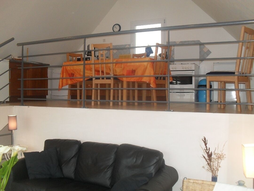 A loft-style living area with a dining table covered by an orange tablecloth, a black leather couch, and a staircase leading to an upper level.