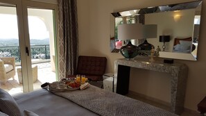Ein Hotelzimmer mit Bett, Frühstückstisch, einer Couch, einem Sessel, Kamin und Balkon mit Aussicht.