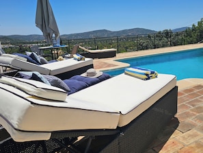 A poolside lounge area with reclining chairs, a table with a bottle, and a view of the mountains.
