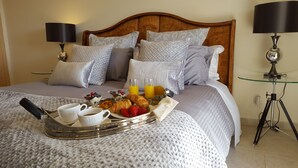 En pænt redt seng med et bakkesæt til morgenmad, blandt andet croissanter, jordbær og juice, i et hotelværelse med en træsenggavl og to sengeborde med lamper.