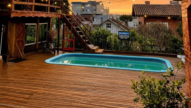 A wooden deck with a swimming pool, a staircase, and a building with a sign for a pool. - Hostel Casa do Rogerio (Caxias do Sul)