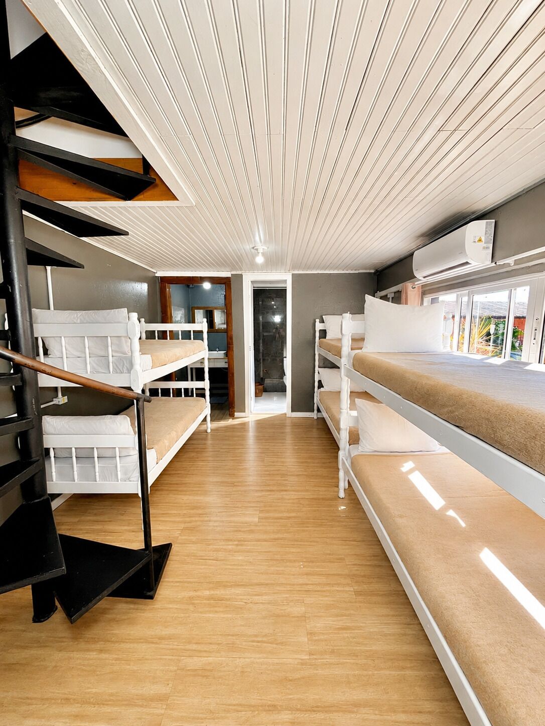 A bunk bed room with a wooden floor, white walls, and a ceiling with white slats.