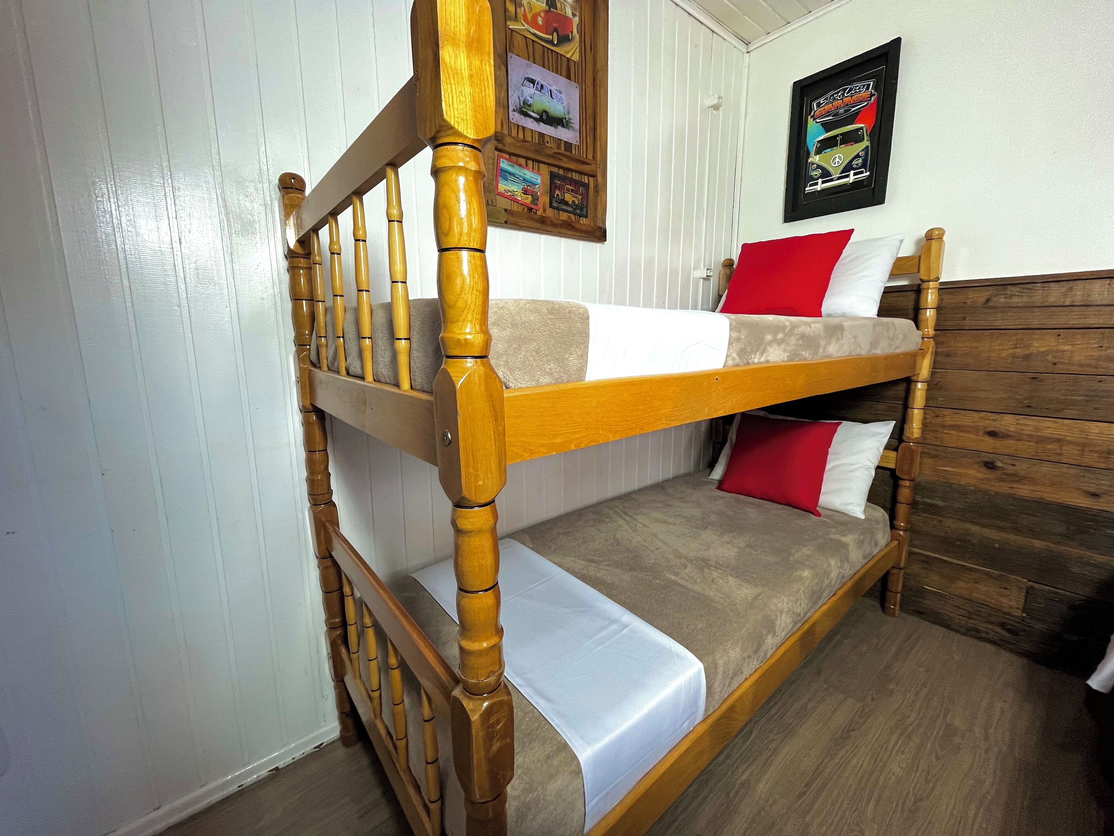 Uma cama beliche com grades de madeira e cabeceira, roupa de cama branca e almofadas vermelhas.