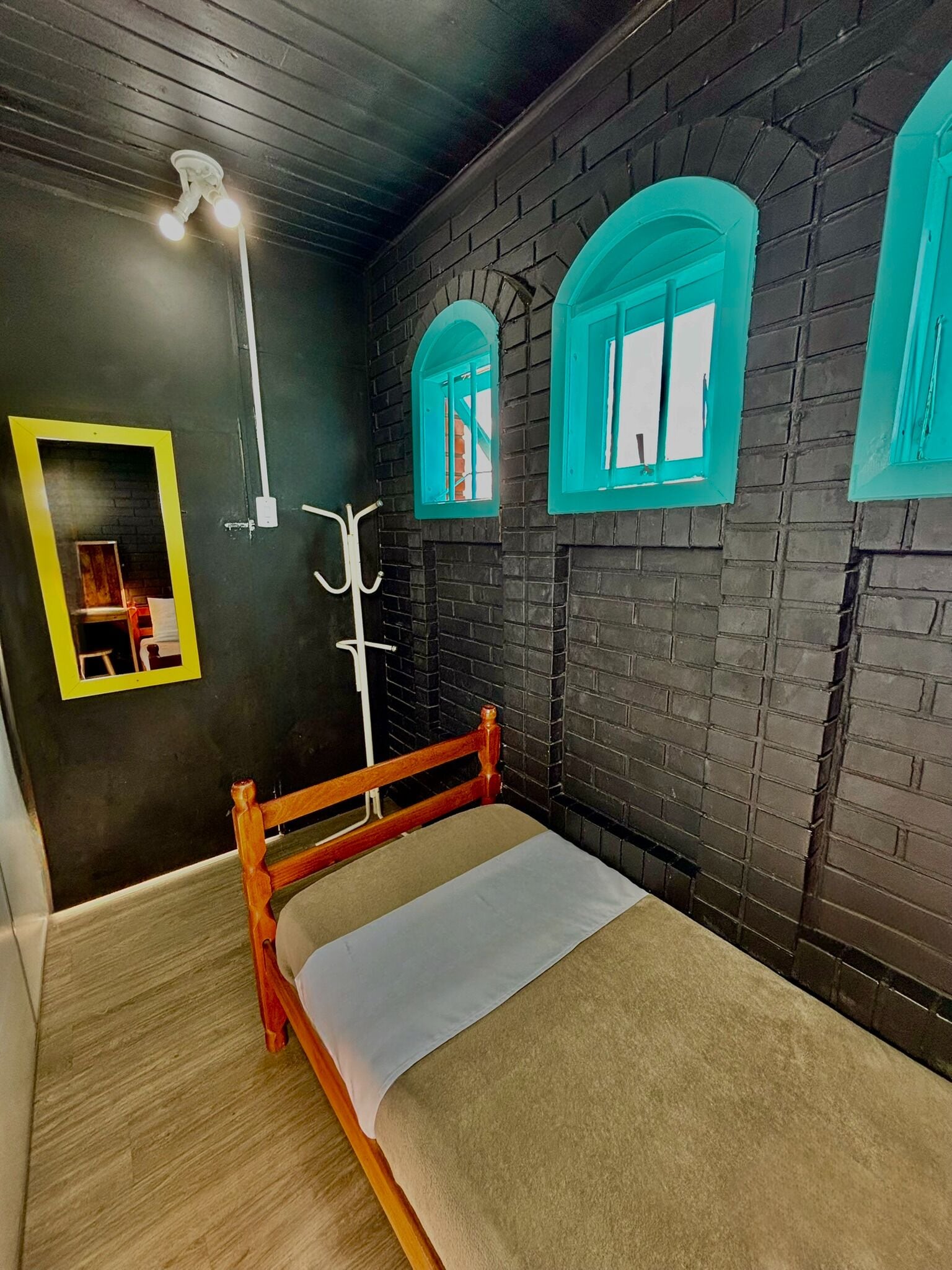 A room with a bed, a wooden bench, a mirror, and a window with a teal frame.