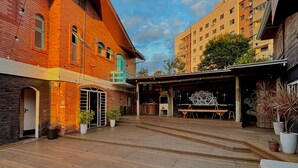 A courtyard with a wooden deck, brick buildings, and potted plants. - Hostel Casa do Rogerio (Caxias do Sul)