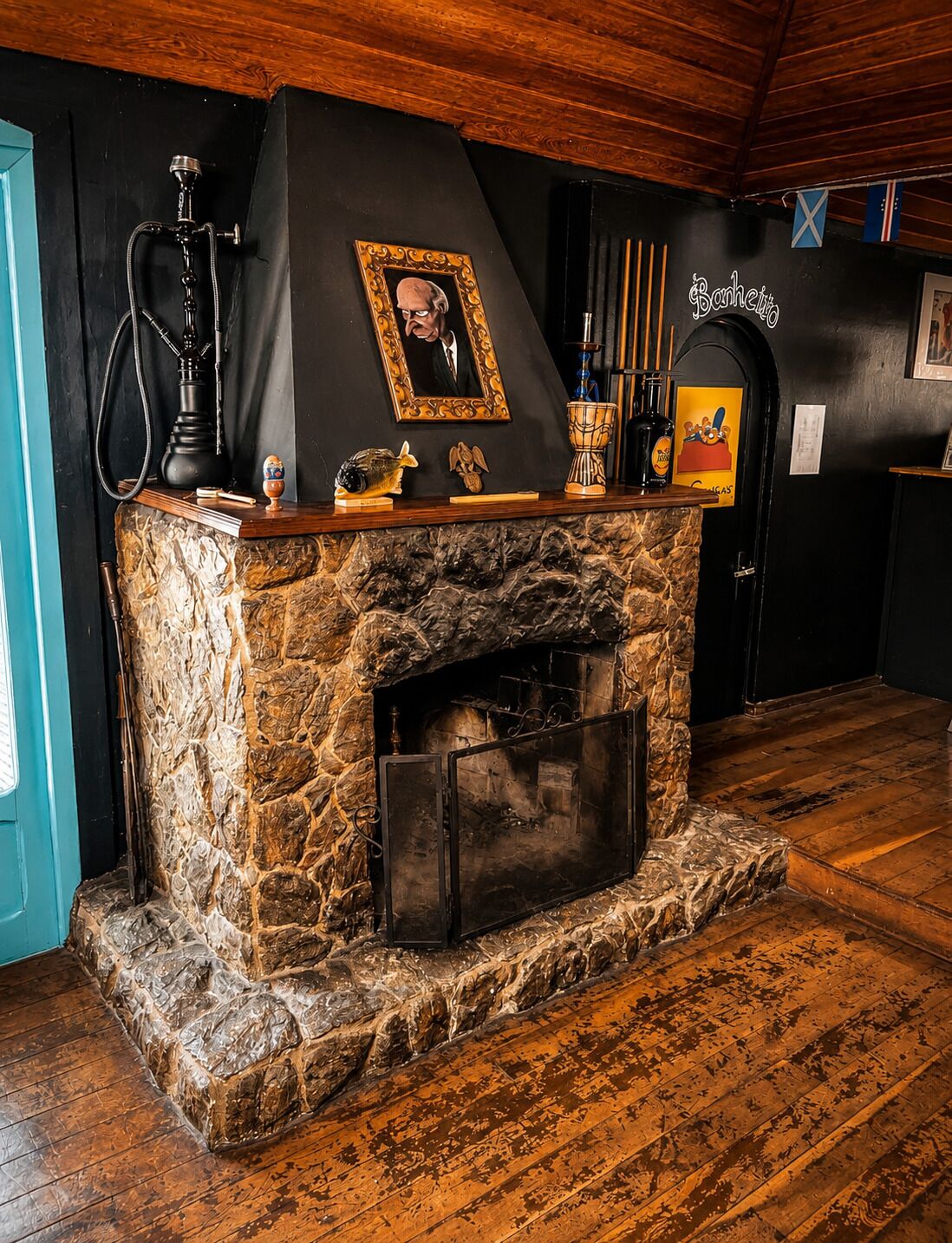 Una chimenea de piedra con repisa negra, un cuadro enmarcado y una botella de whisky sobre la repisa.