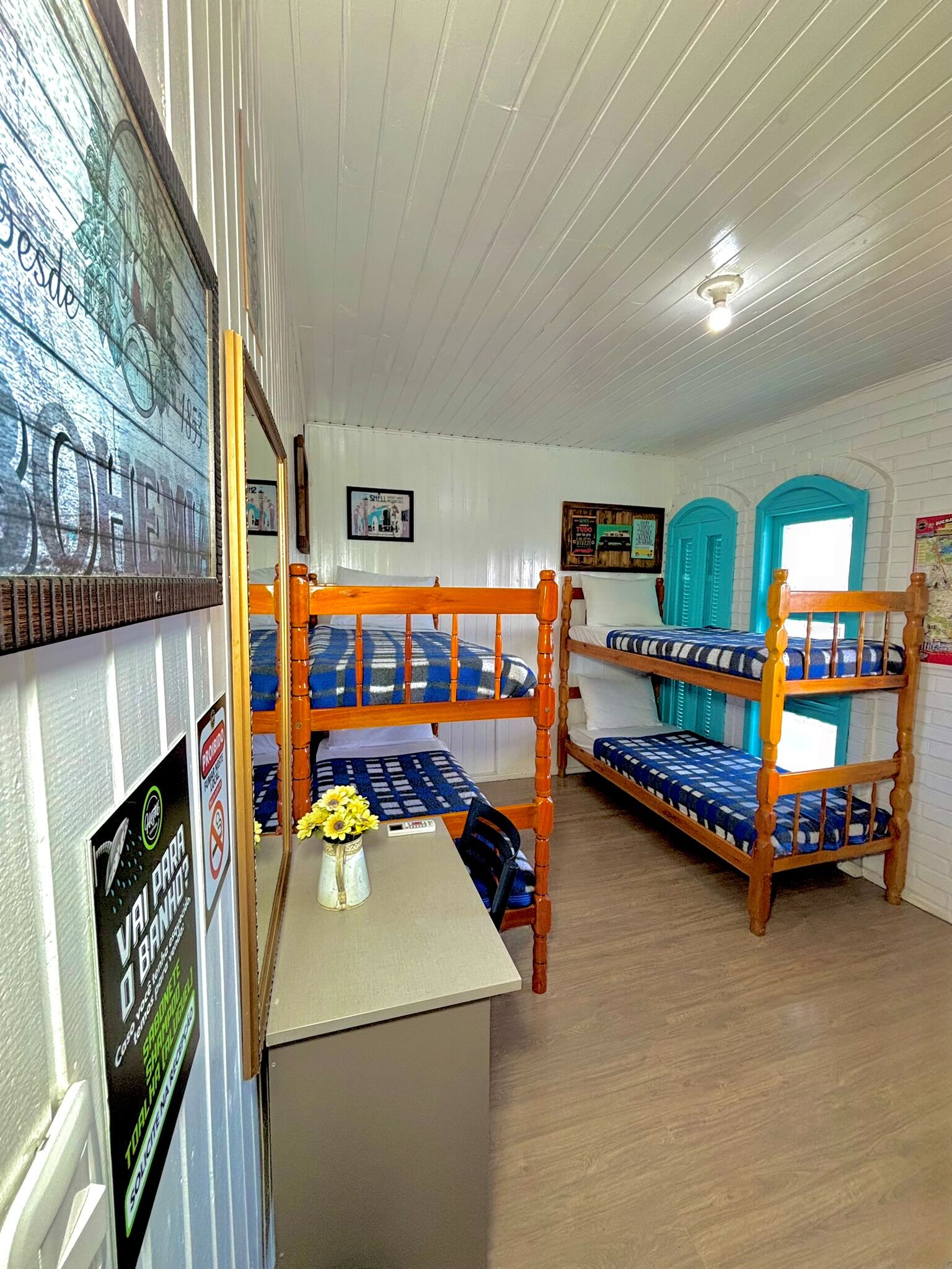 Un dormitorio con literas, una mesita con un florero y un cartel en la pared.