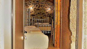 Um corredor estreito que leva a um quarto com parede de pedra, vigas de madeira e uma cama com cobertura branca.