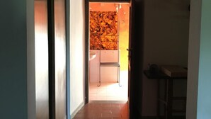 Un pasillo estrecho con suelo de baldosas que conduce a un baño con lavamanos y una silla.