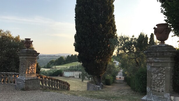Un sendero de grava que conduce a una entrada portonada con pilares de piedra y un árbol alto.