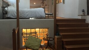 Une pièce chaleureuse avec un lit superposé, un fauteuil près d’une cheminée et un escalier.