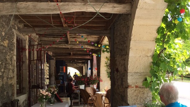 Un espace de restauration en plein air, avec des tables pour deux, abrité par une structure en bois dont les poutres apparentes sont visibles.