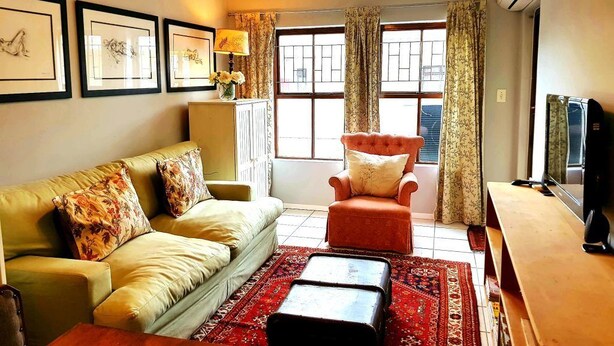 Un salon comprenant un canapé, un fauteuil, un pouf et un téléviseur.