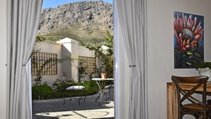 An open doorway leading to a patio with a mountain view, a table with chairs, and a painting of a flower on the wall. - Petit Plaisir Cottage (Franschhoek)