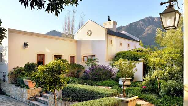 A building with a garden, stone steps, and a mountain in the background. - Petit Plaisir Cottage (Franschhoek)