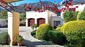 A building with a paved entrance, a covered area with red leaves, and well-maintained bushes. - Petit Plaisir Cottage (Franschhoek)