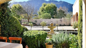 A patio area with a table and chairs, a fountain, and a view of mountains. - Petit Plaisir Cottage (Franschhoek)