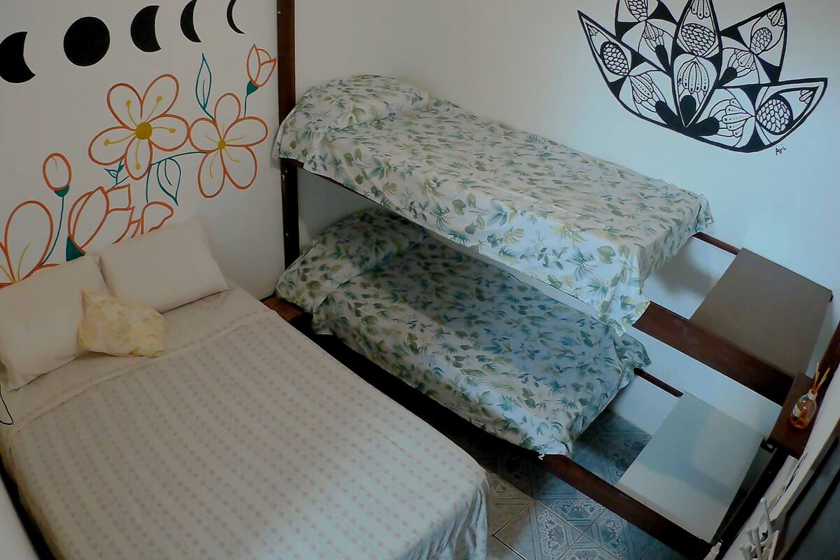 Una habitación pequeña con una cama individual y edredón y almohadas estampadas con motivos florales, una cama nido de madera y un adorno en la pared con flores y lunas.