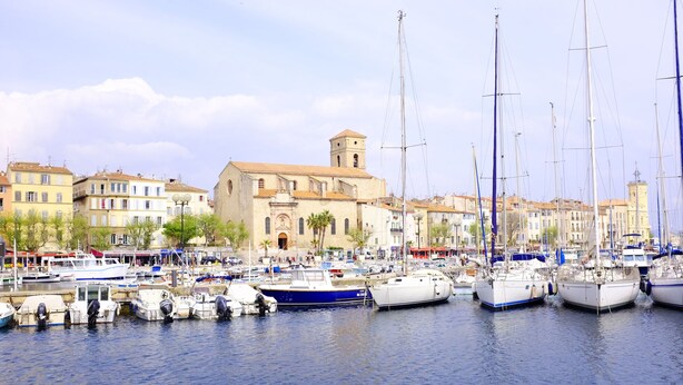 A marina with multiple boats docked, a prominent church with a bell tower, and surrounding buildings. - Modern studio, air conditioning, parking, wifi, terrace, 2 steps from the beach (La Ciotat)