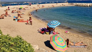 A beach with people sunbathing and swimming, a rocky breakwater, and boats in the water. - Modern studio, air conditioning, parking, wifi, terrace, 2 steps from the beach (La Ciotat)