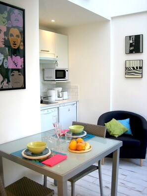 A compact living space with a dining table set for two, a kitchen area with modern appliances, and a cozy seating area with a dark-colored sofa.