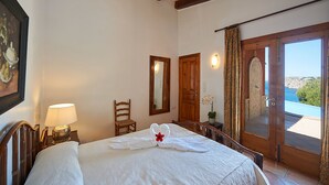 Een hotelkamer met een bed, een stoel, een bureau met een lamp, een spiegel en een deur die leidt naar een balkon met uitzicht op zee.