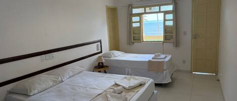 A hotel room with two beds, a window with a view, an air conditioning unit, and a door.