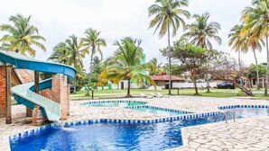 En pool med en vattenrutschkana, palmer och en byggnad av tegel.
