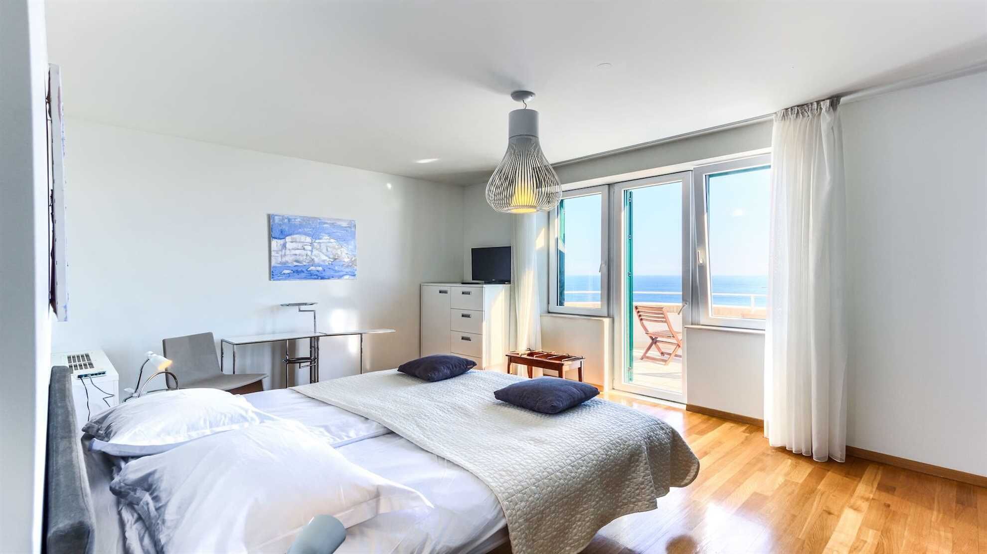 Ein Schlafzimmer mit Bett, Schreibtisch, Stuhl, Fernseher und einem großen Fenster mit Meerblick.
