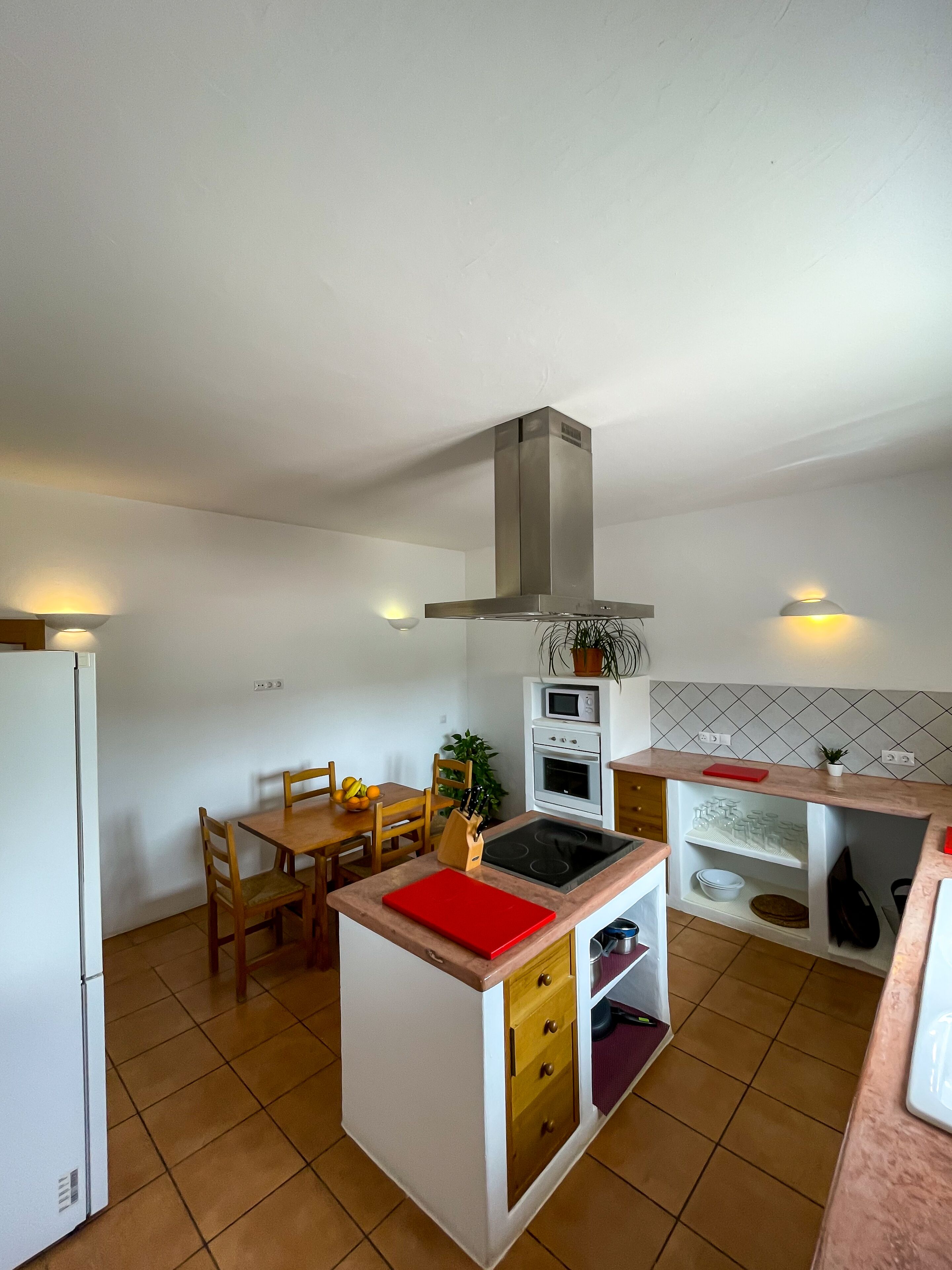 A compact kitchen with a central island, a dining table with chairs, a built-in oven, and a microwave.