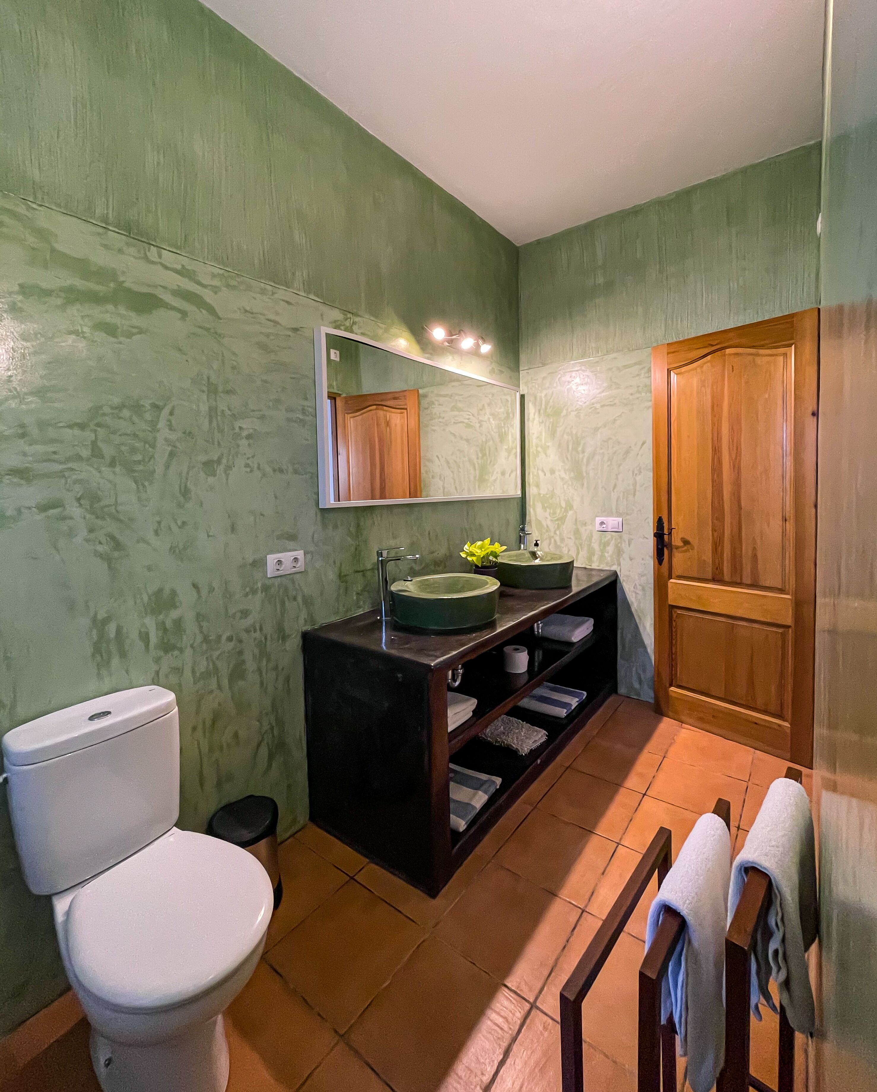 A bathroom with a toilet, sink, mirror, and wooden door.