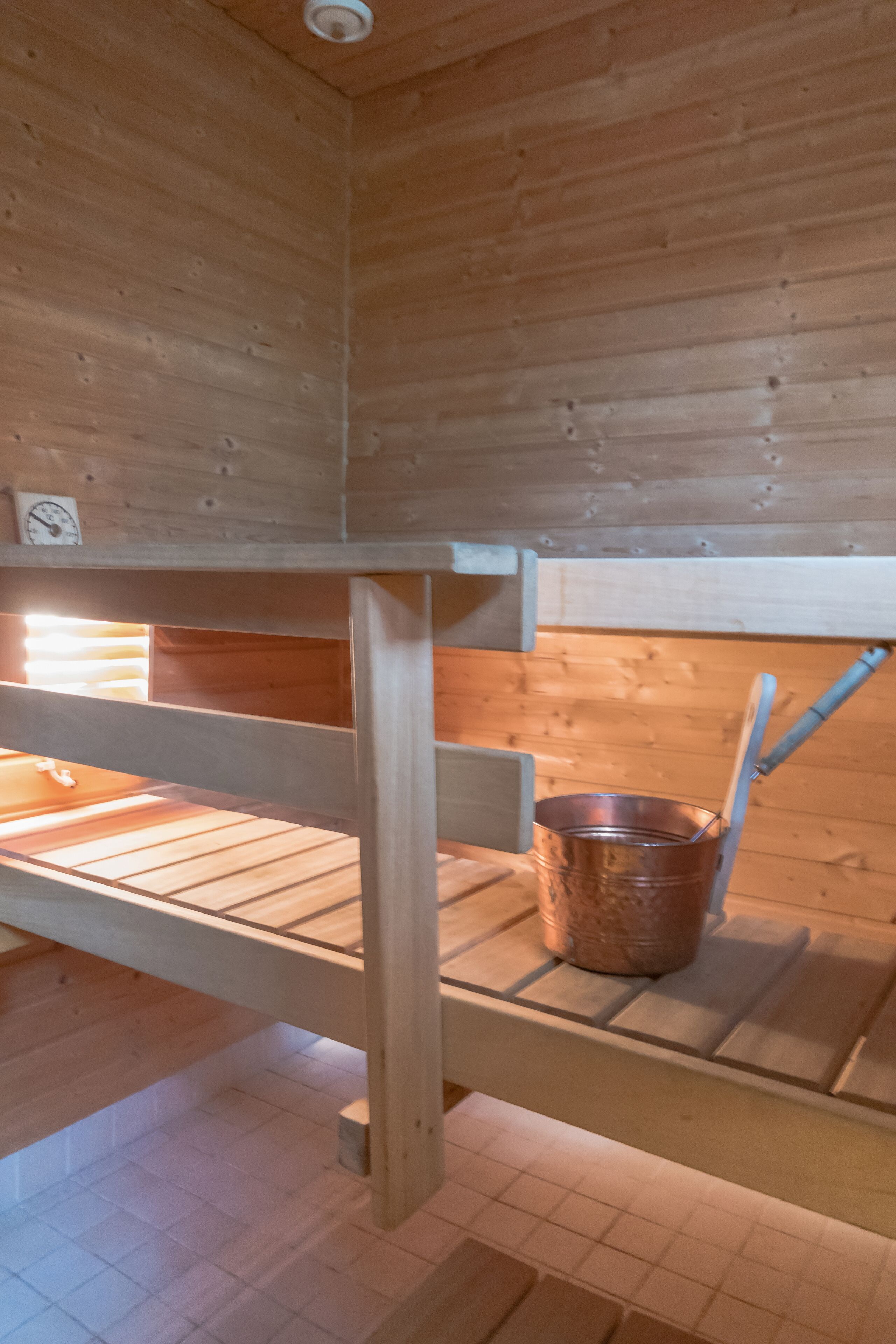 L’intérieur d’une cabane en bois, avec un lit superposé, un seau en métal et une étagère en bois.
