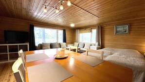 A wooden cabin interior with a dining table, two sofas, a TV, and large windows. - Köningsviken vacations in Sipoo (Sibbo)