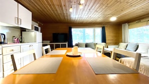 A wooden cabin interior with a dining table, chairs, a TV, and a sofa. - Köningsviken vacations in Sipoo (Sibbo)