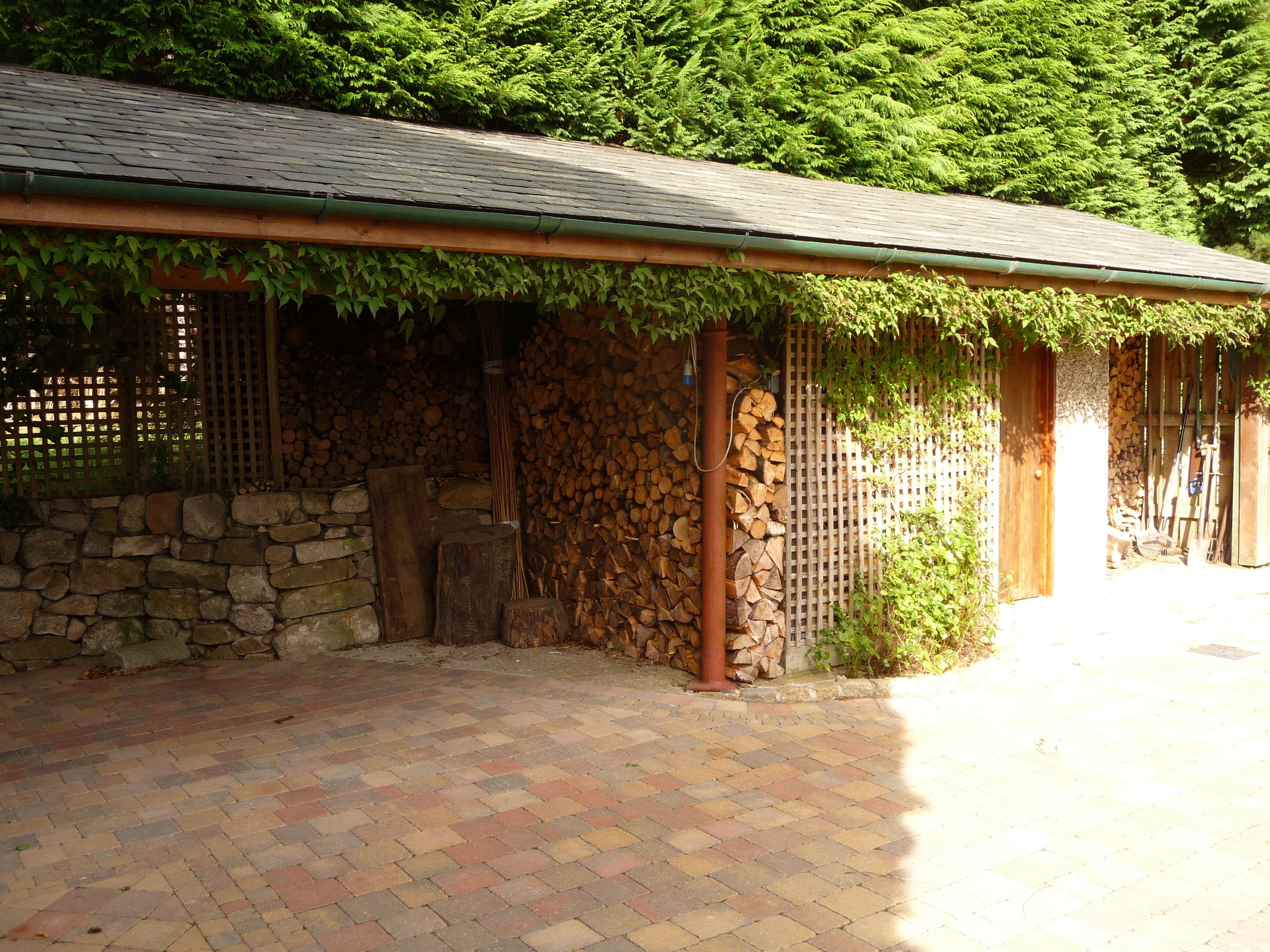 A covered outdoor area with a stone wall, wooden logs, and a brick floor.