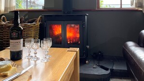 A cozy room with a wooden table, a bottle of wine, and glasses, a fireplace with logs, and a view through large windows.