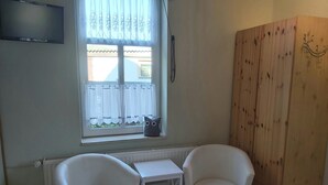 A room with two white chairs, a small white table, a window with white curtains, and a wooden wardrobe.