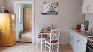 A compact kitchen with a wooden dining table, white chairs, and a small cabinet.
