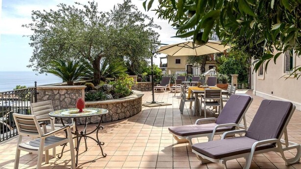 An outdoor patio with a table and chairs, a view of the sea, and a stone wall.
