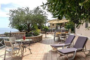 Un patio al aire libre con mesa y sillas, vista al mar y un muro de piedra.