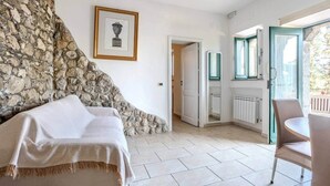 A room with a stone wall, a bed, a framed picture, a door leading to a balcony, and a table with chairs.