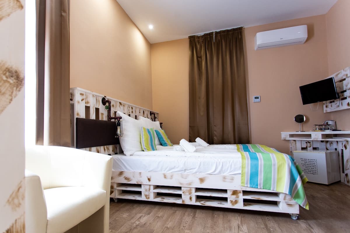 A bedroom with a white bed, a white desk, a flat-screen TV, and a ceiling-mounted air conditioner.