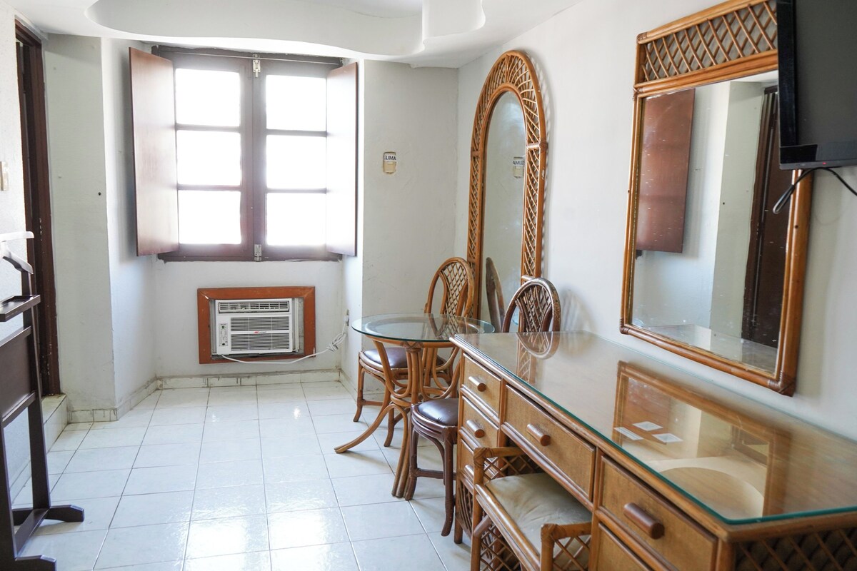 A room with a glass-top dining table, wooden chairs, a large mirror, and a television.