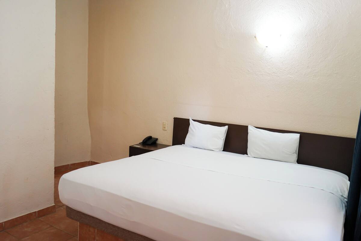 Een net opgemaakt bed met witte lakens in een hotelkamer met effen muren en een klein nachtkastje met een telefoon.