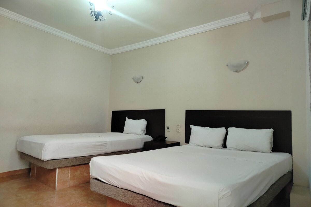 A hotel room with two beds, a nightstand, and a wall-mounted light fixture.