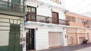 Hotel "Hotel Plaza" met een balkon, een gesloten winkel met luiken en een geparkeerde scooter.