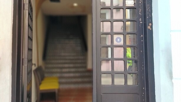 Een hotelentree met een glazen deur, een trap die naar binnen leidt en een bankje buiten.