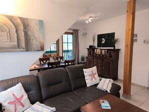 A living room with a dark leather sofa, a wooden coffee table, and a dining area with a table and chairs.
