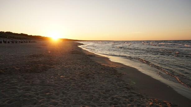 Ein Strand bei Sonnenuntergang, mit sandigem Ufer und Wellen.